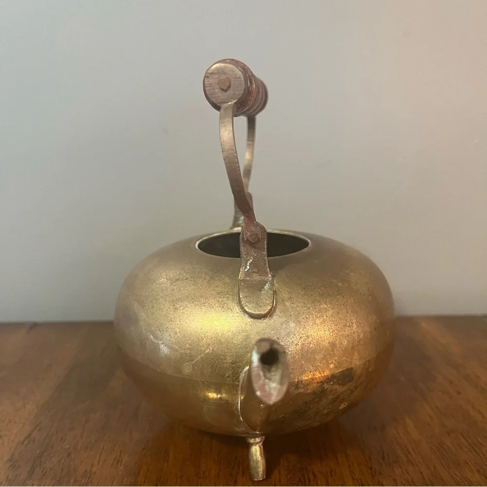 antique brass kettle with a wooden handle and three-legged base.